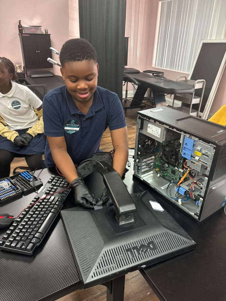 A young student wearing black gloves works with an open desktop computer tower during a hands-on hardware training session
